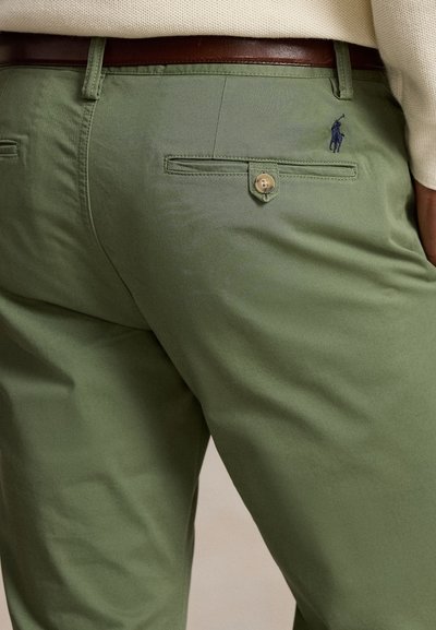 Spodnie w kolorze khaki o gładkiej fakturze, z tylną kieszenią zapinaną na guzik i haftowanym logo nad kieszenią.