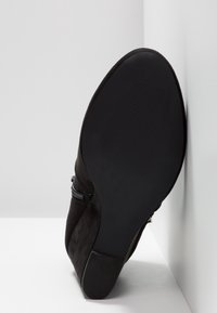 Czarne zamszowe botki za kostkę z teksturowaną gumową podeszwą, detalem zamka z boku i zwężającym się obcasem. Podeszwa jest płaska z subtelnymi rowkami dla lepszej przyczepności.