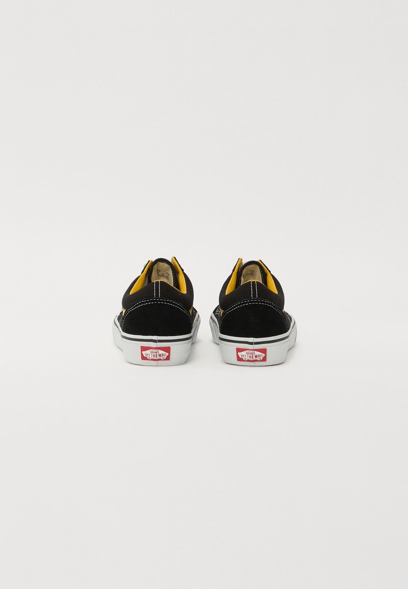 Scarpe slip-on in suede nero con rivestimento giallo e suola in gomma bianca. Presenta il logo Vans rosso sul tallone e cuciture in contrasto.