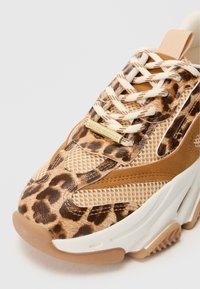 Zapatilla con estampado de leopardo con diseño de malla y ante sintético, en tonos beige y marrón, puntera redonda y suela blanca. Detalle de logotipo en dorado.