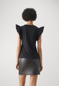 Camiseta negra con mangas cortas volantes, diseño ajustado, combinada con una minifalda de cuero negra. Textura suave con costuras visibles.