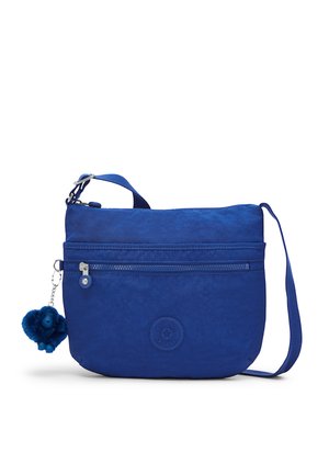 Sac bandoulière bleu avec sangle réglable, poche avant zippée et un petit porte-clés singe bleu et duveteux attaché à la fermeture éclair.