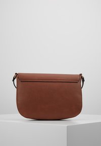 Hnědá kožená taška přes rameno zaobleného tvaru s plochým klopou a jemným prošíváním. Obsahuje tenký, nastavitelný popruh s kovovými akcenty.