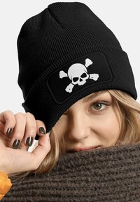 Black knit beanie with a white skull and crossbones graphic patch. The beanie features a ribbed texture and a snug fit.