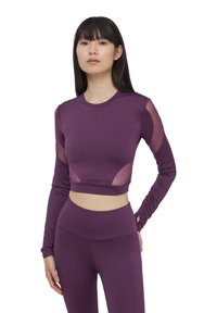 Top cropped a maniche lunghe viola con pannelli in rete sulle spalle, texture liscia, scollatura rotonda, design aderente, abbinato a leggings coordinati.