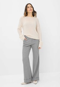 Lichtbeige gebreide trui met lange mouwen, gecombineerd met grijs gestreepte wijde broek met een getailleerde pasvorm en opgerolde boorden.