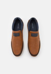 Zapatos marrones sin cordones con un upper texturizado, acentos en un marrón más oscuro y un forro interior en navy con la marca 'Pier One'.