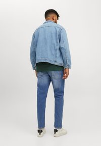 Leren spijkerjack in lichtblauw, met een klassieke kraag en knoopsluiting. Gecombineerd met blauwe jeans en witte sneakers, met een groen shirt eronder.