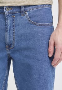 Siniset farkut suorilla lahkeilla, joissa on viisi taskua, vetoketjullinen edestä ja kuparinvärinen ommel saumoissa.