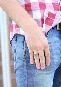 Denim jeans met een lichte wassing, met een rechte broekspijp. Een hand rust op de zak en draagt een metalen ring. Rood-wit geruit overhemd zichtbaar.