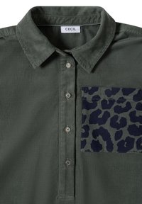 Chemise en velours côtelé vert foncé avec des boutons et une poche à motif animalier sombre sur le côté gauche sous le col.