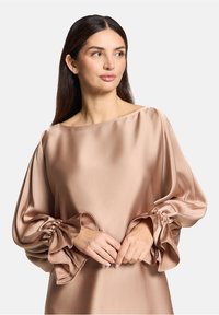 Blushfarbene Satinbluse mit einem Bootsausschnitt, Puffärmeln und gerafften Rüschendetails an den Manschetten. Glatte Textur überall.