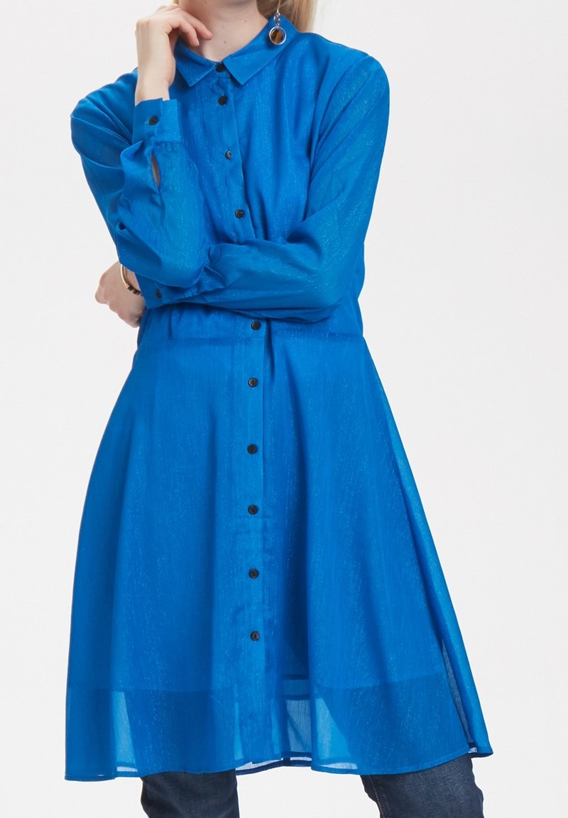 Robe chemise bleue avec col, tissu transparent, manches longues et boutons noirs. Présente une silhouette fluide et des manches à poignets.