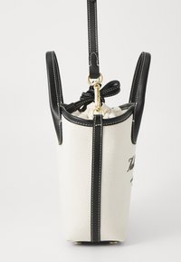 Kangastoot, millel on must nahkdetailid, köitmise sulgus ja kuldne riistvara. Omab kontrastõmblusi ja struktureeritud kuju.