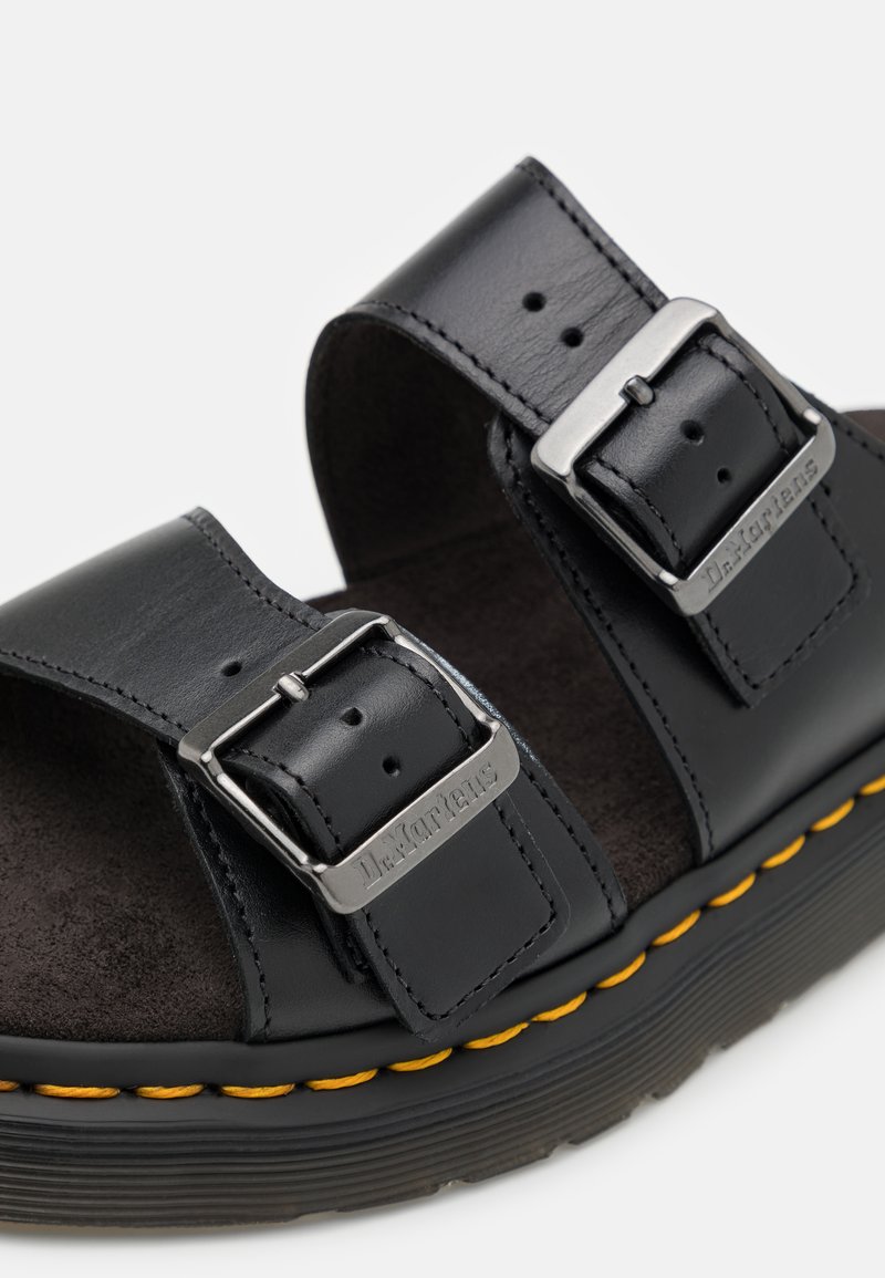 Black leather sandals with two adjustable straps, silver buckles, and yellow stitching on a textured black sole.
