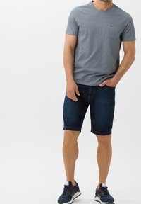 Harmaa lyhythihainen T-paita, jossa on rintatasku, yhdistettynä polvenpituisiin tummansinisiin farkkushortseihin ja tummiin urheilukenkään.