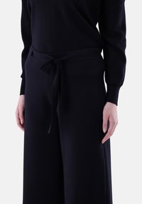 Marineblaue Strickhose mit weitem Bein, ausgestattet mit einem Stoffgürtel, der an der Taille gebunden ist. Glatte Textur mit lockerer Passform um die Beine.
