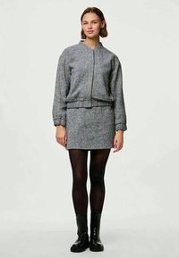Siva bomberska jakna z ujemno krilo, ki se ponaša s strukturo, rebrastimi manšetami in gladko teksturo. V kombinaciji z črnimi gležnjarji.