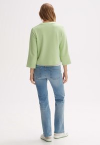 Haut vert à manches courtes avec un large décolleté, associé à un jean bleu clair et des baskets blanches avec des accents verts. Tissu lisse et coupe décontractée.