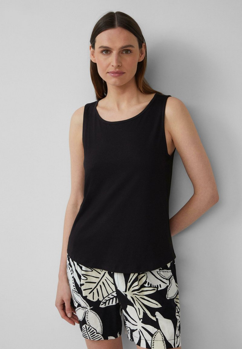 Haut sans manches noir avec un col rond, fabriqué en tissu lisse. Assorti à un short à motifs avec un feuillage blanc sur fond noir.