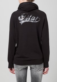 Felpa nera con collo alto e maniche lunghe. Presenta un logo argentato sul retro e un tessuto liscio e strutturato.