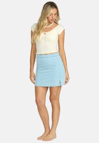 Falda de mezclilla azul claro con una ligera abertura lateral, que cuenta con un diseño ajustado y una cinturilla de altura media. Tejido texturizado con costuras visibles.