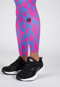 Blå och rosa mönstrade leggings i elastiskt tyg, ihop med svarta sneakers med vita detaljer och logotyp.