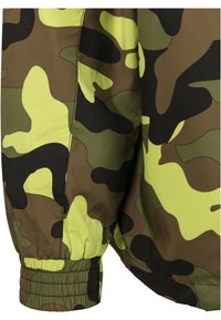 Kamouflagejacka med ärm i brun, svart och neongrön. Har samlade elastiska manschetter och en slät, glänsande tygtextur.