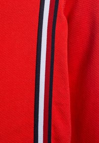 Červená pletená látka s vertikálními pruhy v bílé, námořnické modři a tmavší červené. Textura je měkká a mírně žebrovaná.