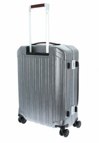 Valigia rigida argentata con scanalature verticali, manico in alluminio estensibile e quattro ruote nere. Comprende chiusure sicure e dettagli decorativi.