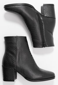 Pár černých kotníkových bot s texturovaným hadím vzorem, blokovými podpatky a bočním zipem, zobrazených z bočního pohledu a z pohledu na podešev na bílém pozadí.