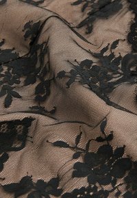 Țesătură din dantelă florală neagră cu o textură fină de plasă pe un fundal bej deschis, având modele intricate și designuri florale detaliate.