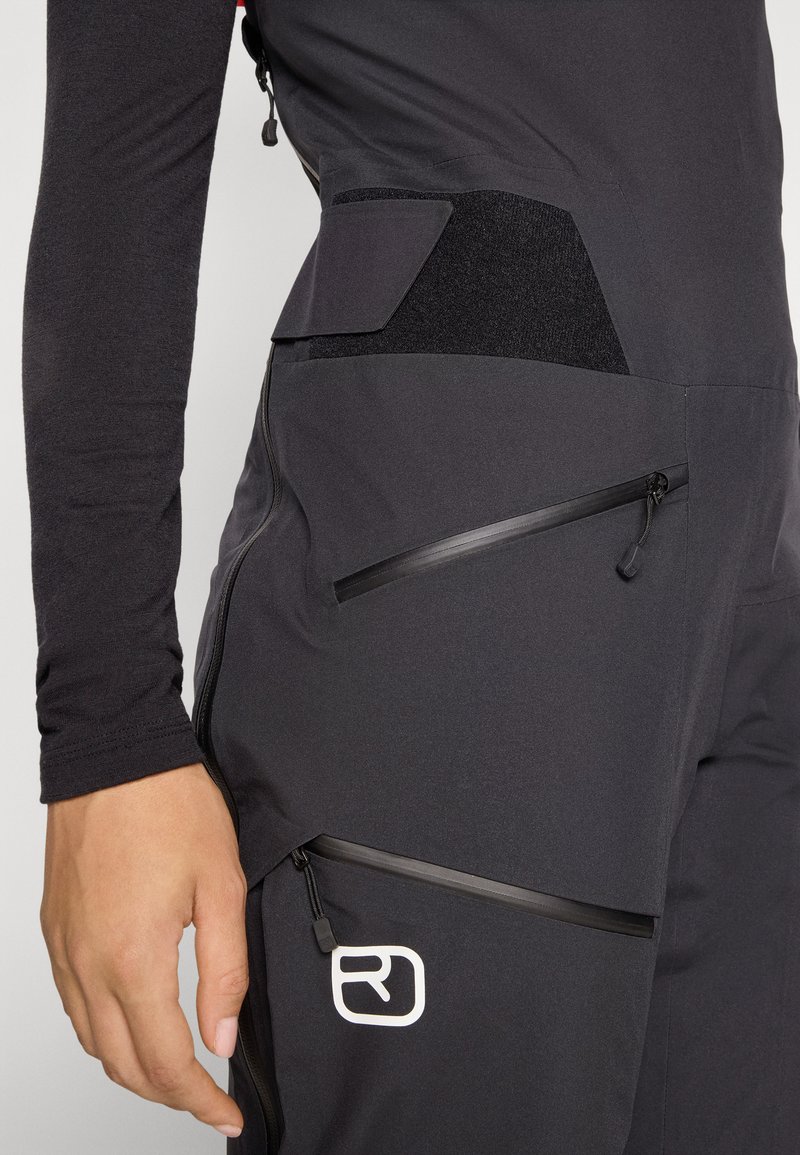 Schwarze Sporthosen mit mehreren Reißverschlusstaschen, strukturierten Stoffakzenten und einem Logodetail. Sie verfügen über ein eng anliegendes Design.