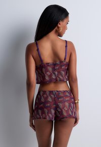Ensemble de haut court et de shorts à motif avec un design de feuilles violet, rouge et or. Tissu lisse avec des bretelles ajustables et une silhouette courte.