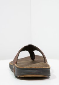 Brune skinnsandaler med tåpost, teksturert fotseng og en fleksibel svart gummisåle. Synlige perforeringer forbedrer pusten.