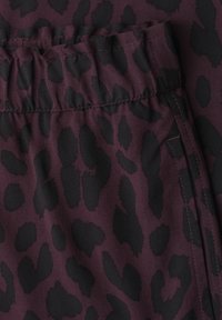 Gros plan d’un tissu avec fond violet foncé et motif léopard noir irrégulier, avec une ceinture élastique et une couture cousue.