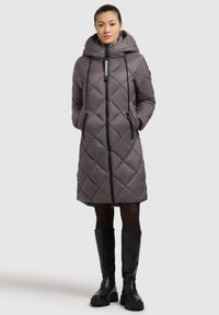 Quilted grey puffer coat with a hood, featuring a full zipper, drawstring accents, and side pockets, paired with black knee-high boots.