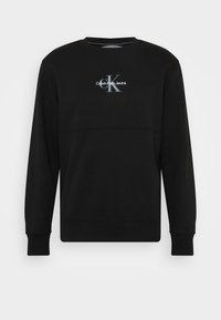 Svart sweatshirt i mjukt tyg med rund halsringning och ribbade muddar. Fram på mitten syns en grå logotyp: "Calvin Klein Jeans."