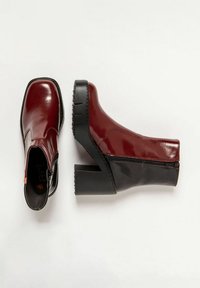 Botines de charol burdeos con un tacón grueso negro, cremallera lateral y textura suave. Punta redondeada con un ligero brillo.