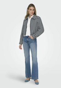Sacou alb-negru cu model houndstooth, cu guler, asortat cu blugi evazați de culoare albastru deschis și pantofi cu toc albaștri.