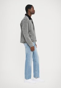Veste en denim grise avec col noir, coupe décontractée. Jean droit bleu clair et baskets blanches. Design simple, peu de détails.