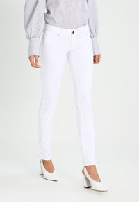 Jeans ajustados blancos hechos de denim, con una textura suave, diseño estándar de cinco bolsillos y una bragueta con cierre de botón metálico.