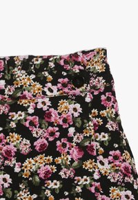 Schwarz gestreifter Cordstoff mit einem lebhaften Blumenmuster in pink, weiß und gelb, der einen schwarzen Knopf am Bund hat.