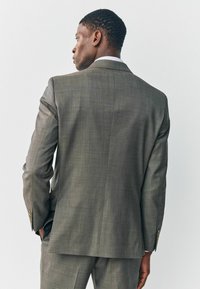 Grau strukturierte Anzugsjacke von hinten betrachtet, mit einem einfachen Schlitz, weichen Schulterpolstern und geknöpften Manschetten, kombiniert mit passenden Hosen.