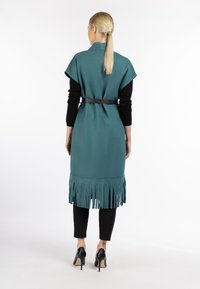 Teal geklede buitenstof met een kraag, tailleriem, gecombineerd met zwarte broeken en hoge hakken. Gladde textuur met een relaxed fit.