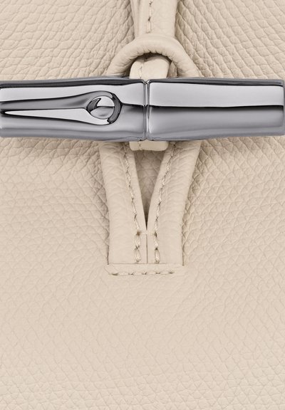 Beige textured leather with a smooth, shiny silver hardware detail. The leather features a delicate quilted pattern and stitched accents.