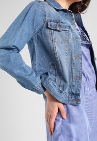 Jeansjacka med ljusblå tvätt, knappstängning framtill, bröstfickor och en klassisk krage. Långärmad med manschettdetalj.