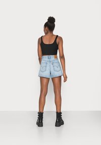 Top corto negro de canalé y pantalones cortos de mezclilla azul claro con un parche marrón en la parte trasera, combinados con botines negros.