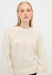 Maglione color crema con lavorazione a maglia testurizzata caratterizzato da perle decorative lungo le spalle e un motivo a foglia. Collo rotondo.