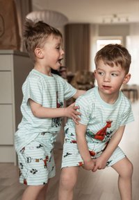Två barn har på sig matchande ljusblå randiga pyjamasar med djurillustrationer. Tyget ser mjukt ut och shorts har lekfulla motiv.